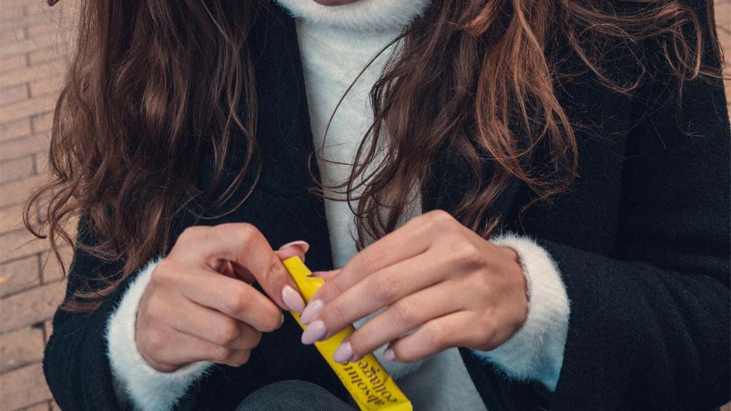 Photo showing a woman with long brunette hair, her face is not visible in the shot but her hands are and she is holding a yellow Absolute Collagen sachet